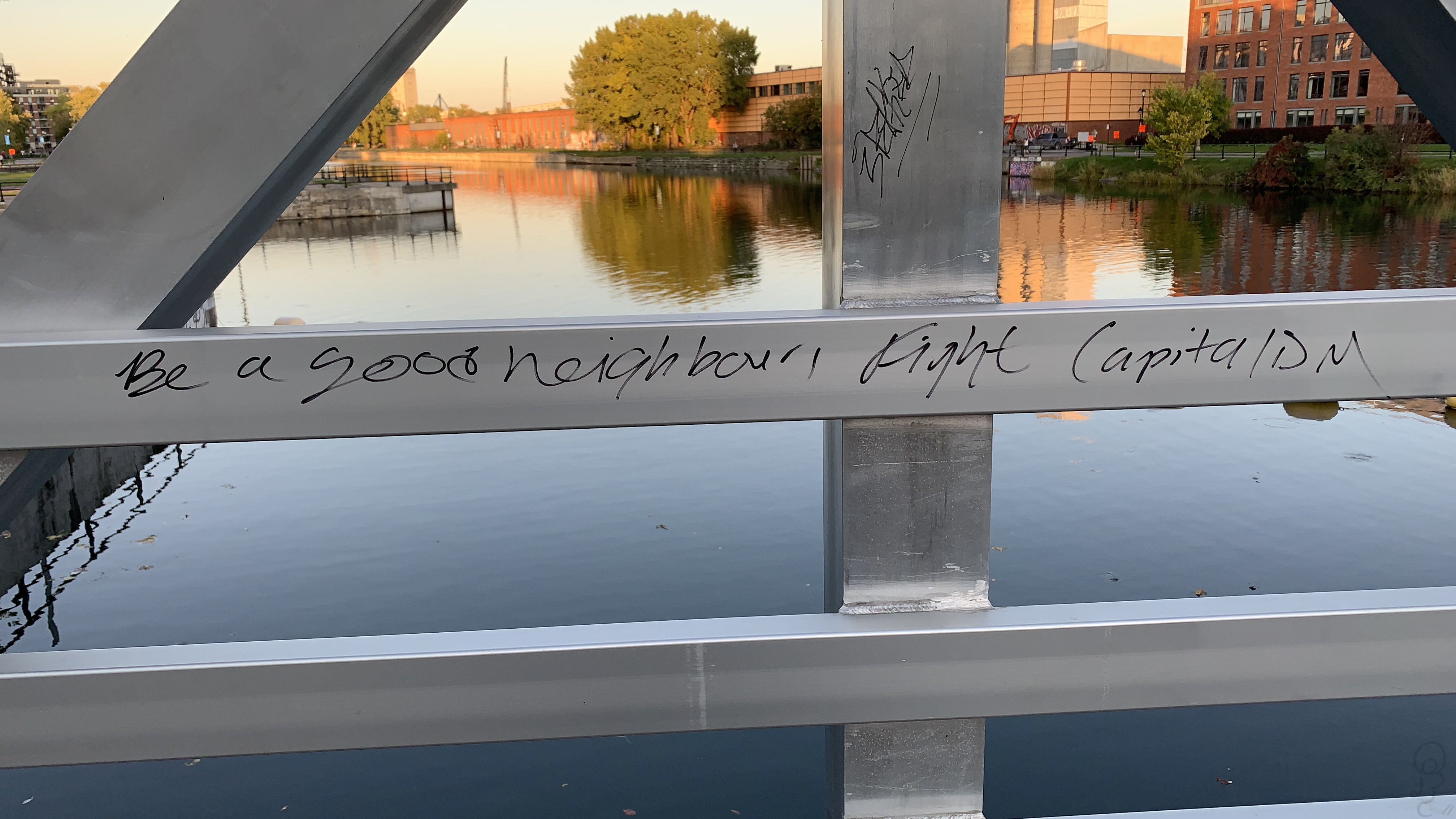 An image of Handwritten sharpie on the side of a metal bridge reading: 'Be a good neighbour, fight capitalism'