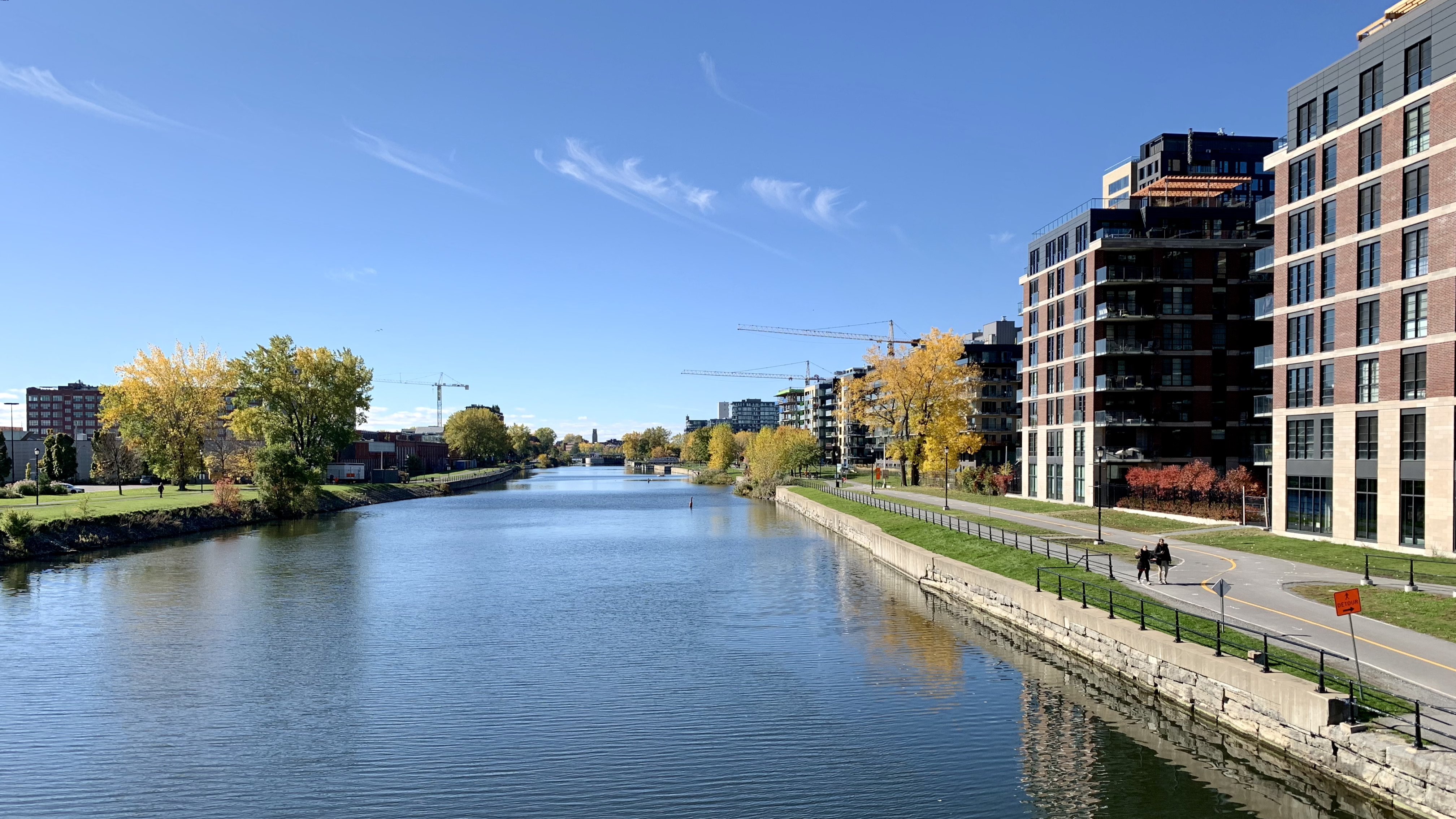 An image of A canal in Montreal, multiple tower cranes are doing building work of some kind.